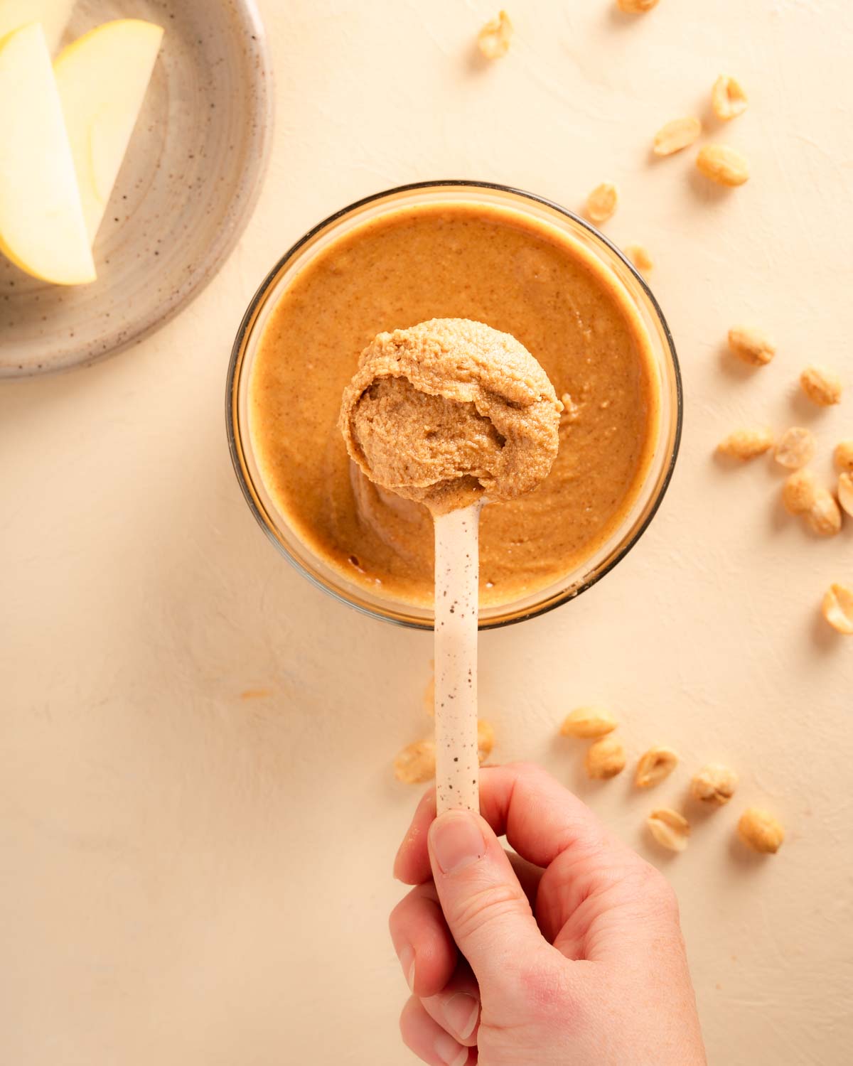 A hand holding a ceramic spoon with thick and creamy Vanilla Cinnamon Peanut butter on the spoon.