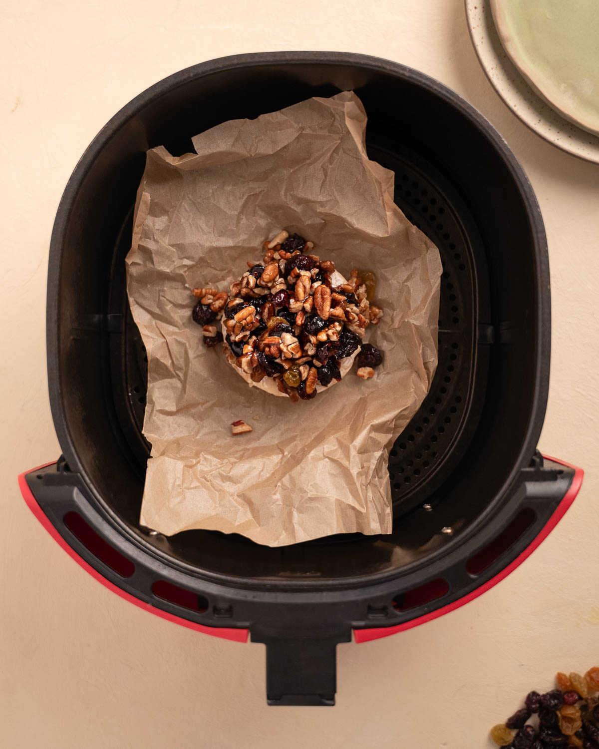 Camembert Cheese topped with dried fruits and nuts in an air fryer basket. 