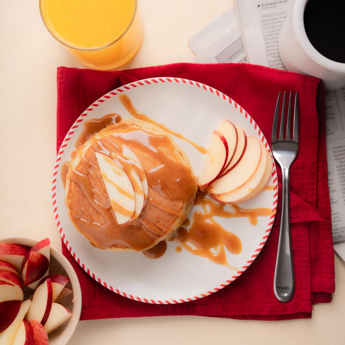 Full sized sweet cream pancakes drizzled with maple peanut butter syrup with sliced apples, orange juice, and coffee.