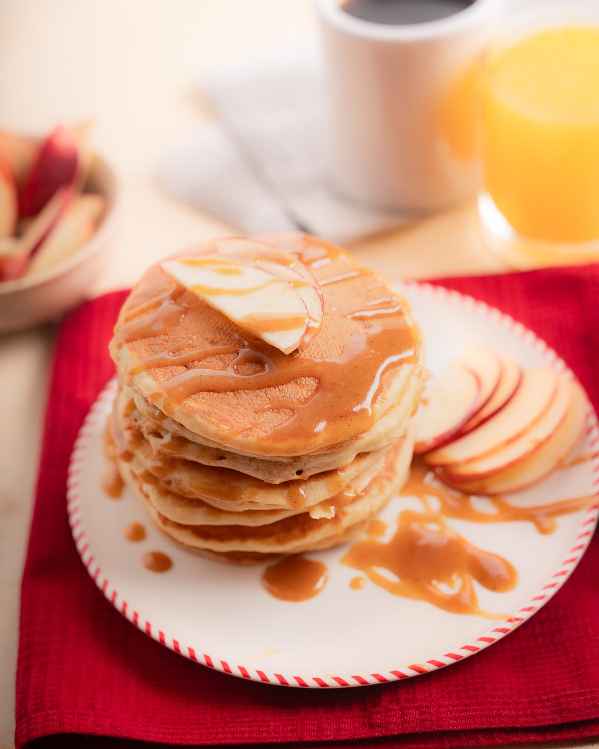 Regular sized pancakes in a white plate with red stripes covered with a maple peanut butter drizzle.