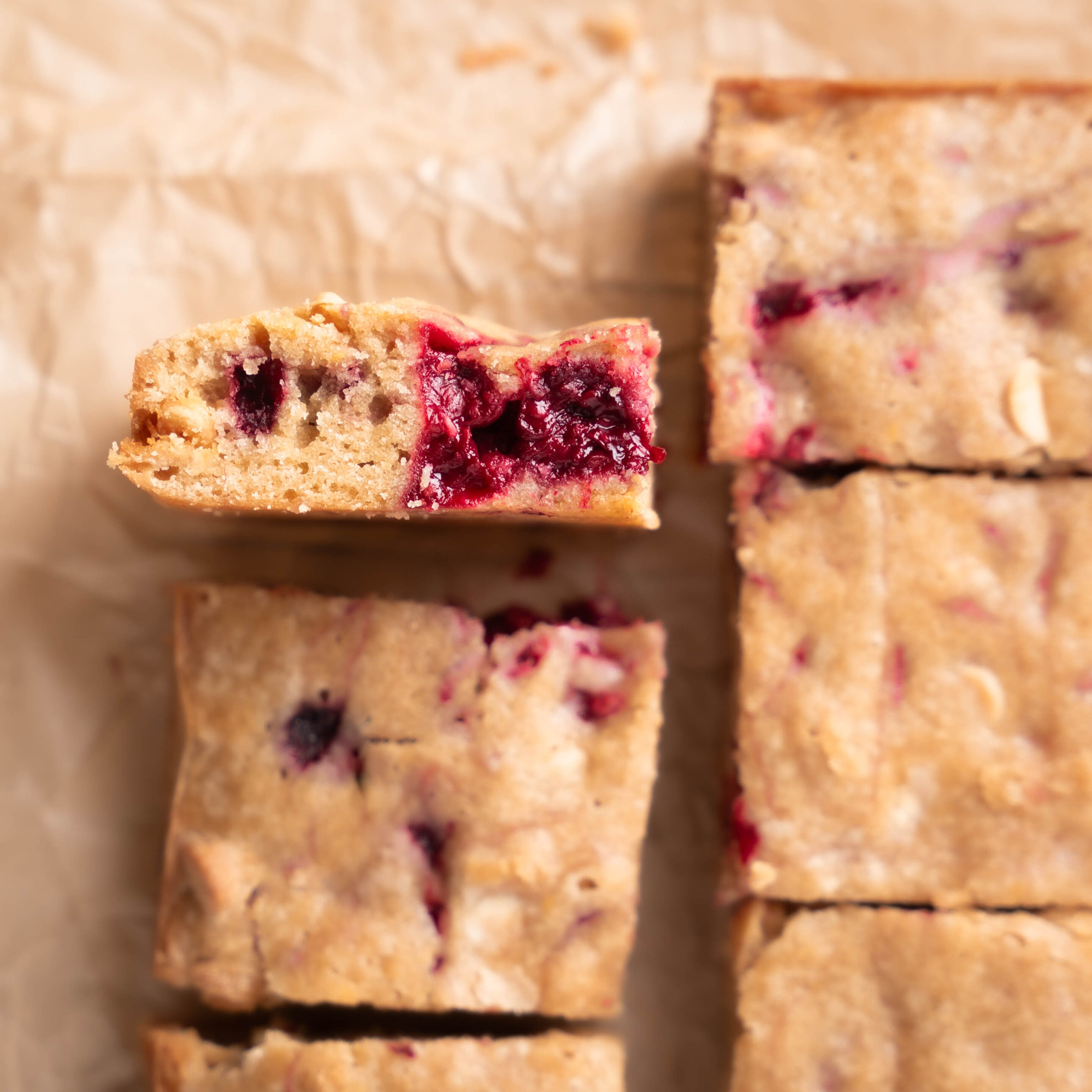 Blondies with raspberries and white chocolate chips, a blondie is turned on its side to show the add ins. 