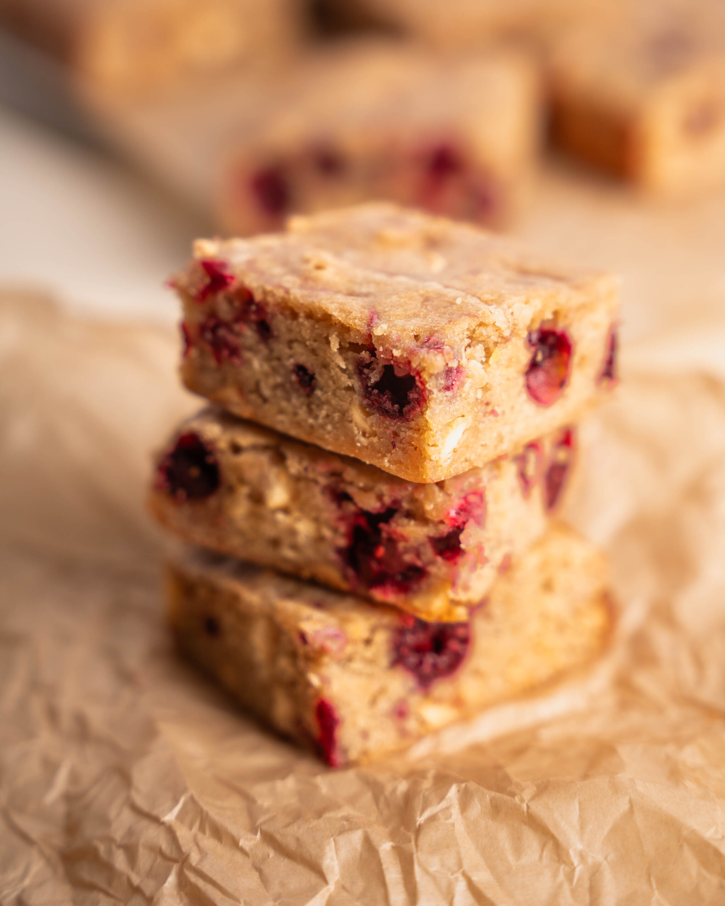 Three Raspberry White Chocolate Blondies stacked on light brown parchment paper.