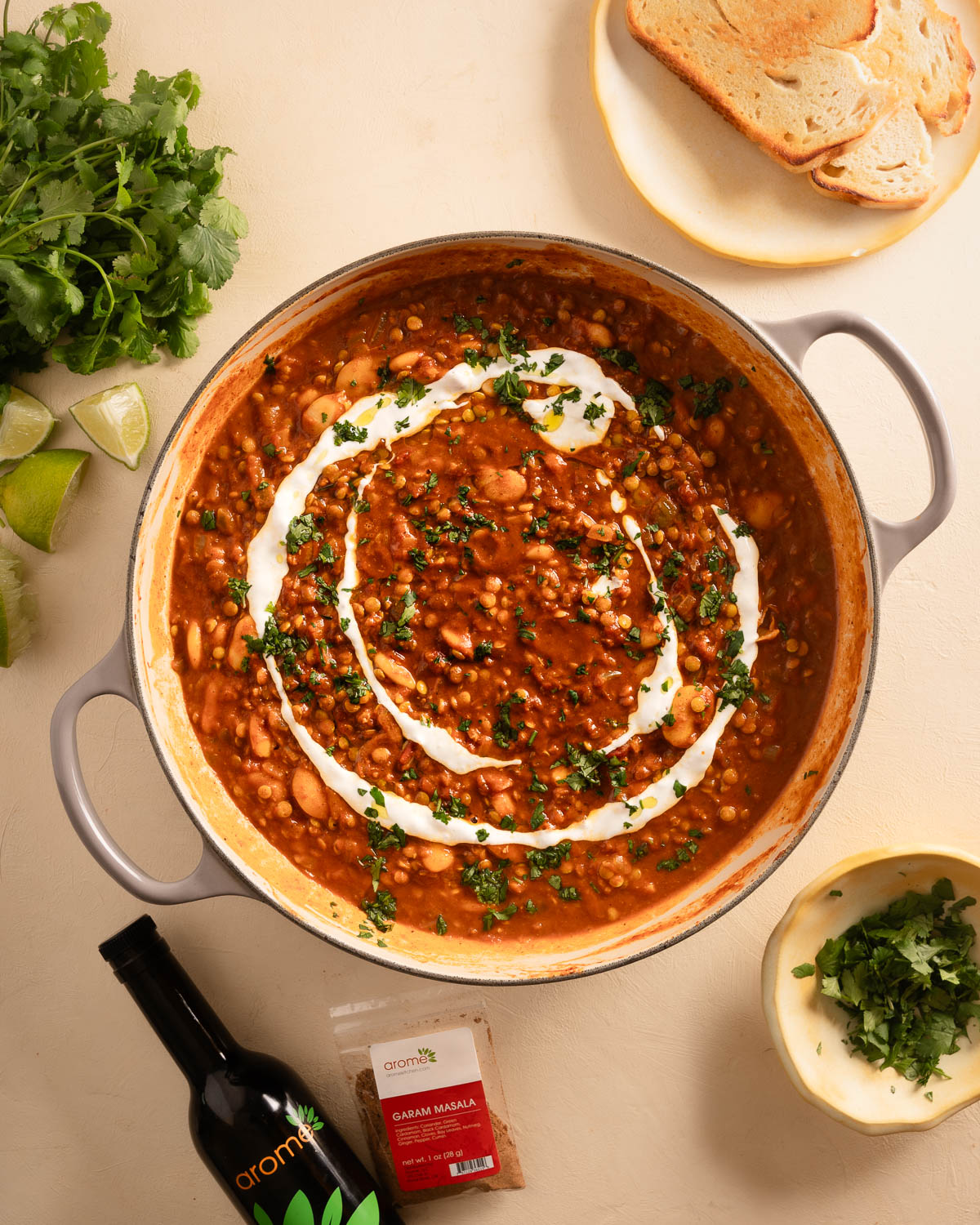 Butter Bean Curry with Lentils in a large shallow cast iron casserole dish with toast, herbs, and Arome spices and oil as props