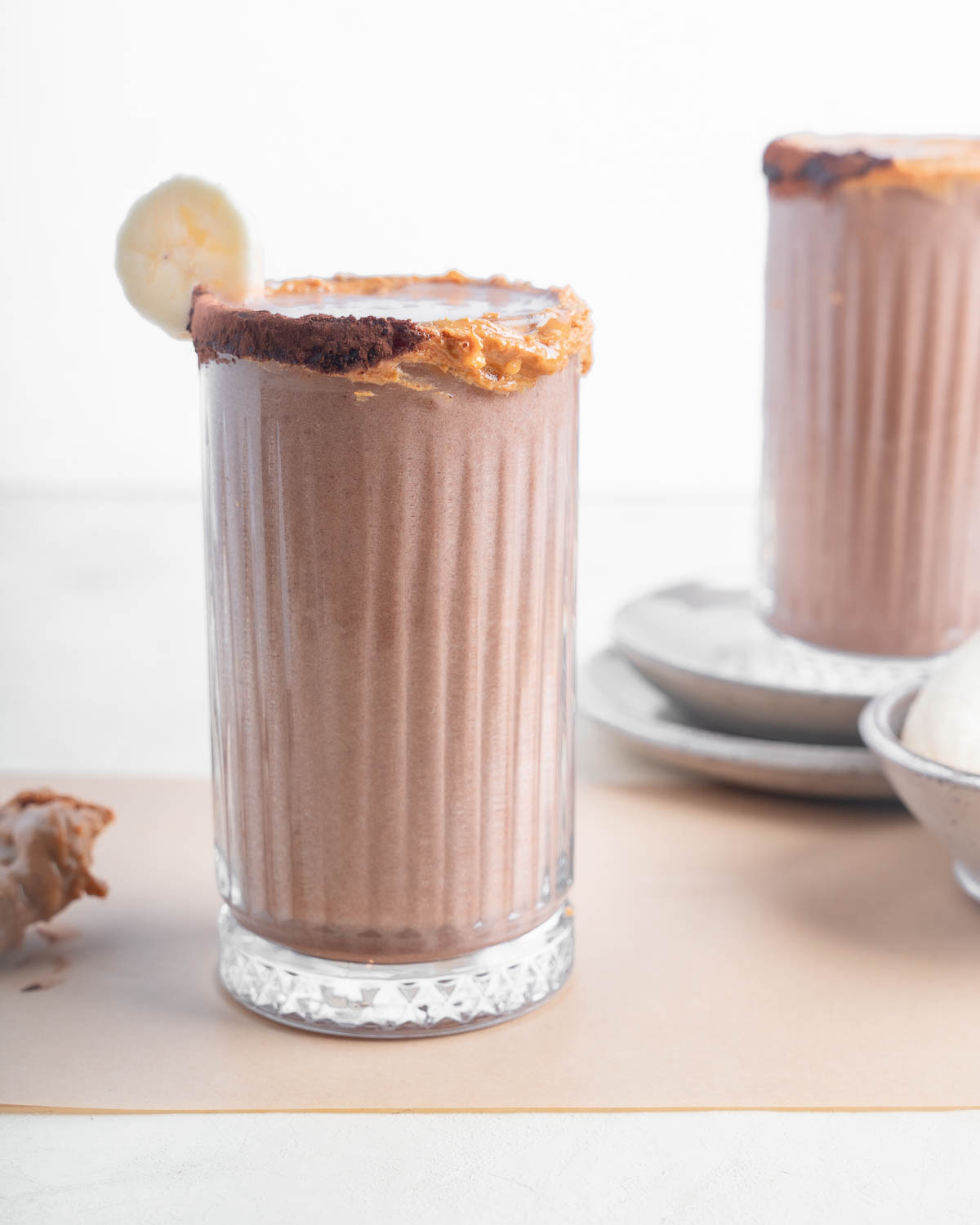 Peanut Butter Cup Tropical Smoothie Cafe Copy Cat straight on shot of the smoothie in a glass with a banana garnish and a peanut butter cocoa powder rim