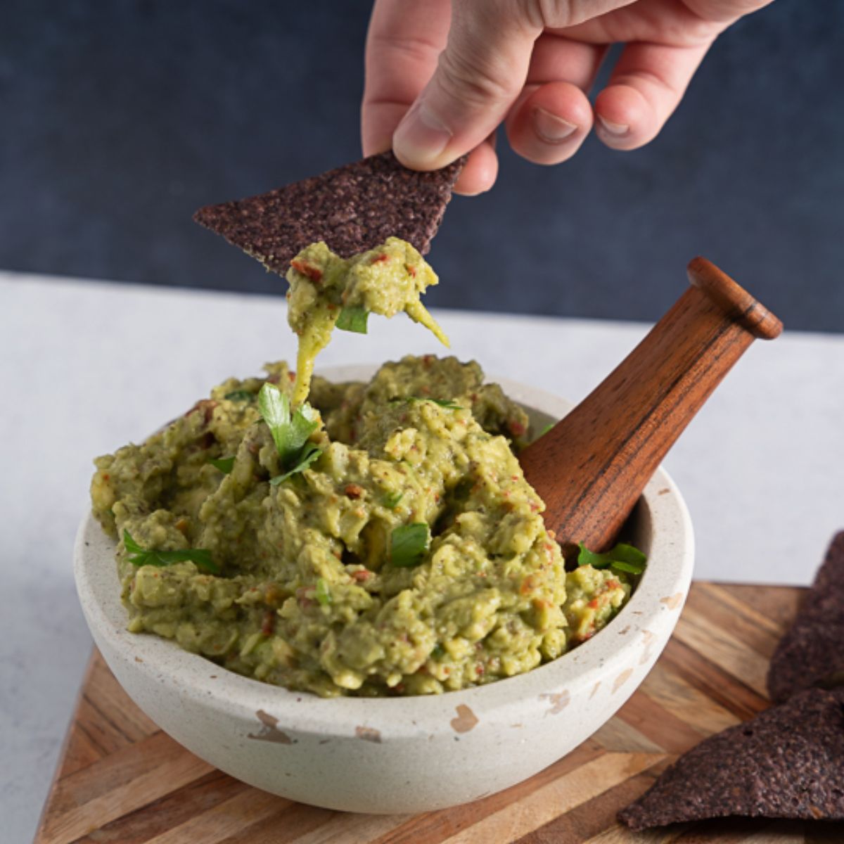 a chip pulling away from a guacamole bowl with guacamole on the chip