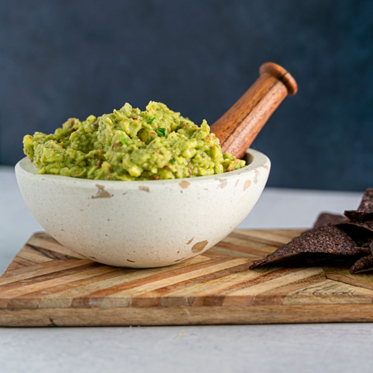 Guacamole in a stoneware bowl with blue corn tortilla chips to the right