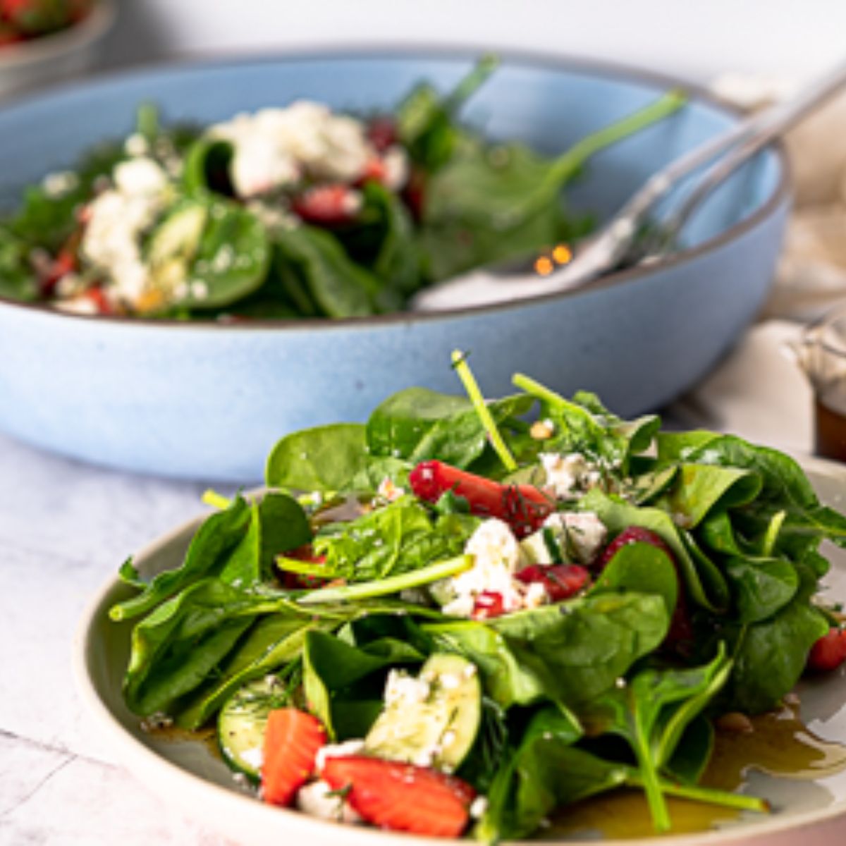 Spinach Strawberry Salad on a plate with a large blue serving bowl with salad behind it