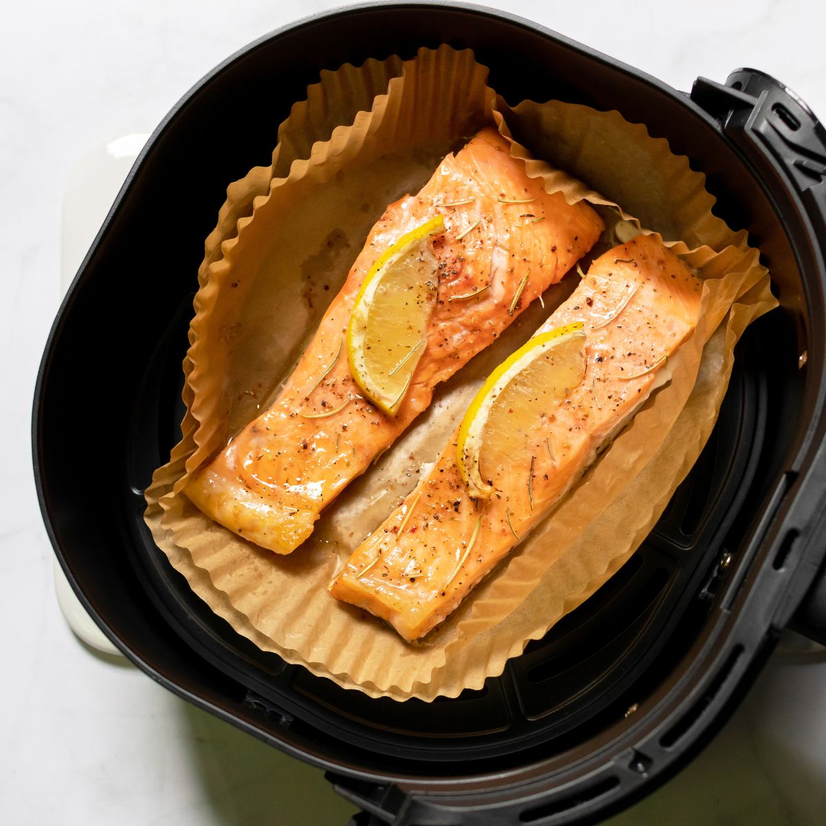 air fryer basket with two salmon fillets with lemon