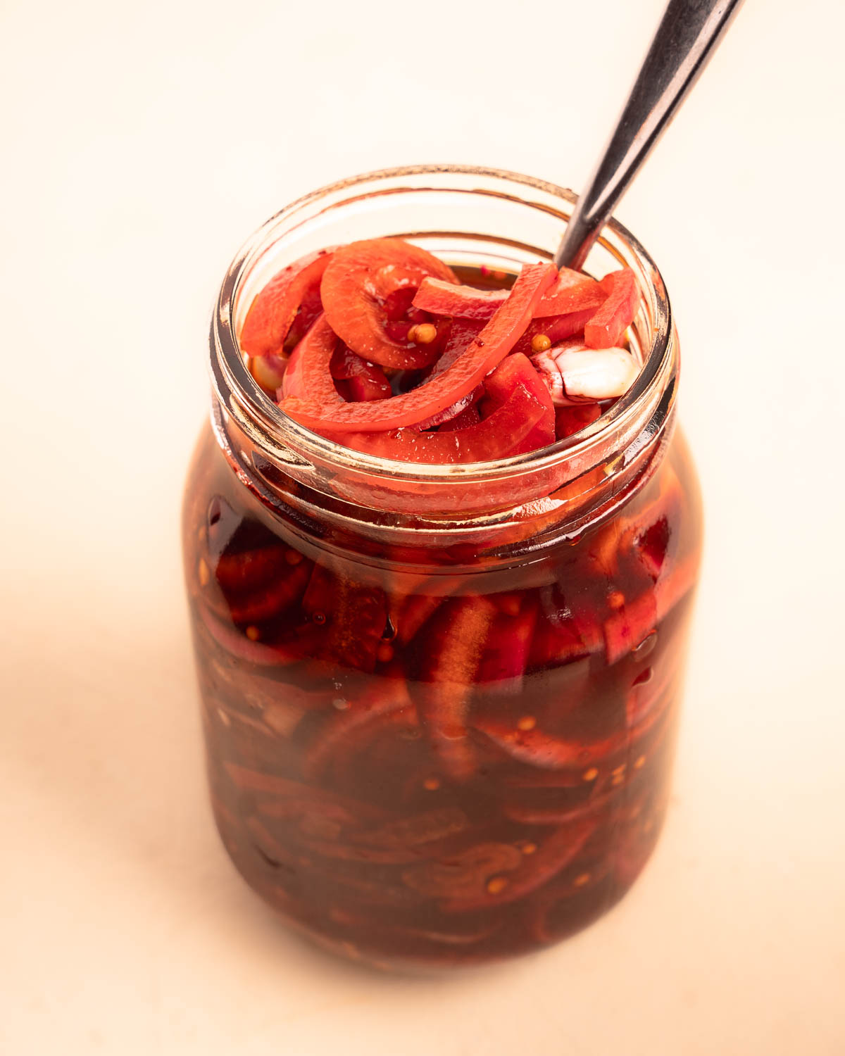 Red Balsamic Pickled Onions in a mason jar with a spoon on an off white background