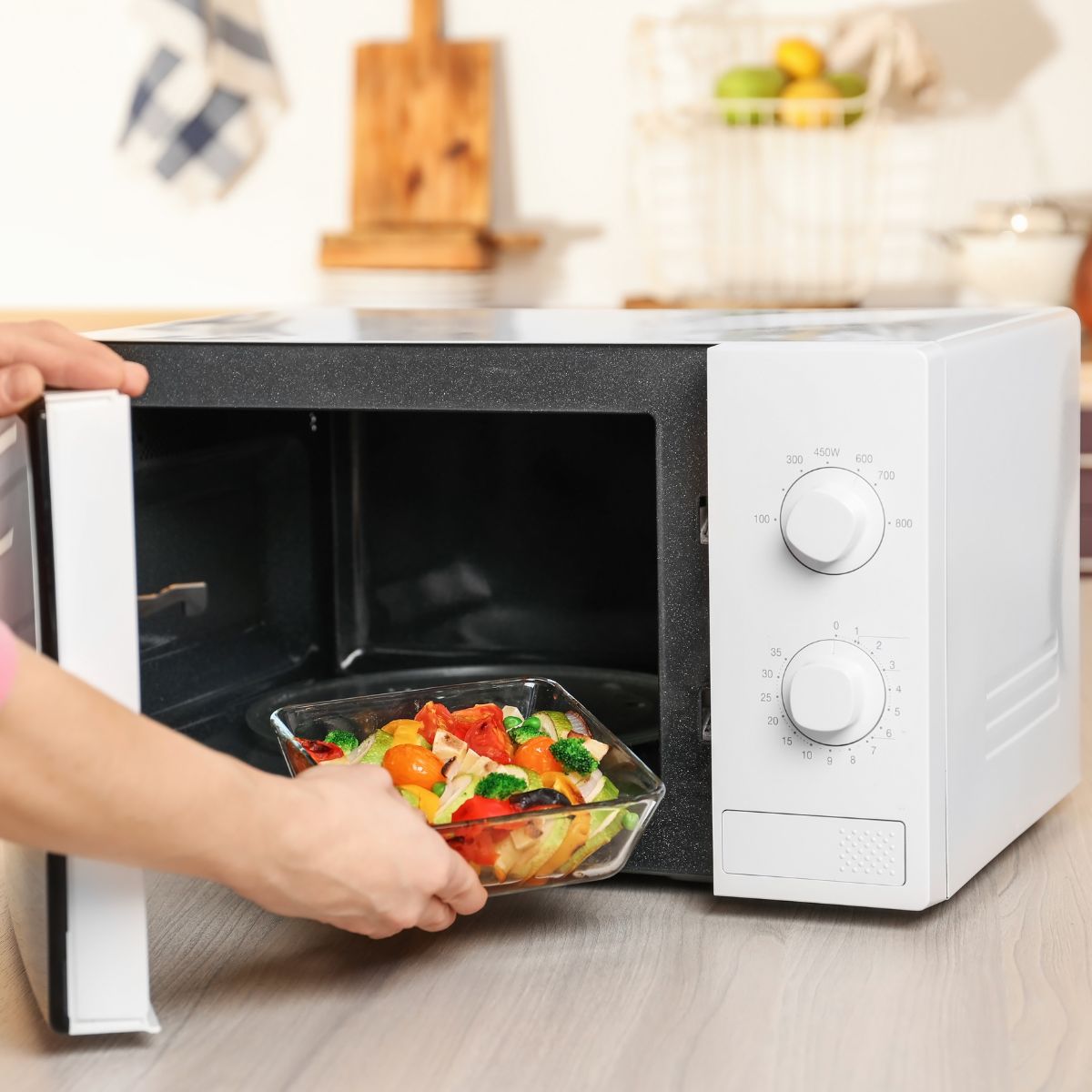 a person placing a bowl of vegetables in a microwave oven