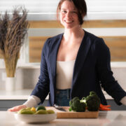 Sarah Harper in her kitchen with a cutting board, broccoli, carrots, and a fruit bowl.