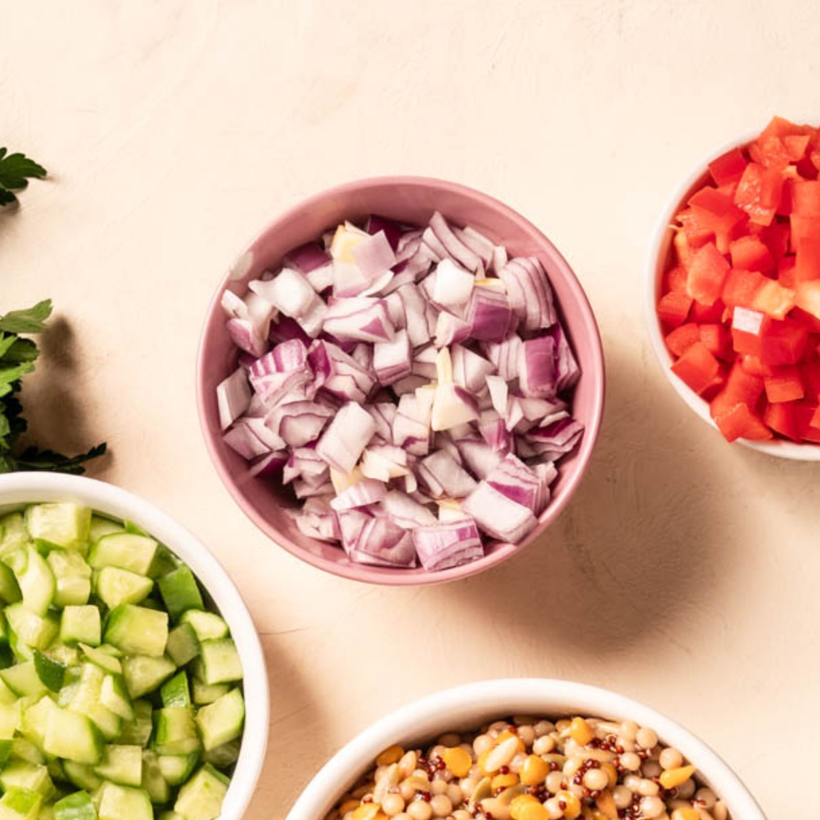 red onions in a pink bowl with other chopped veggies in bowls out of frame