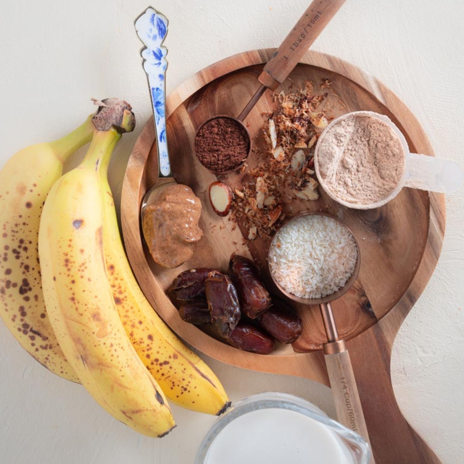 Ingredients for a Smoothie with bananas, nut butters, cocoa powder, protein powder, dates, and nuts