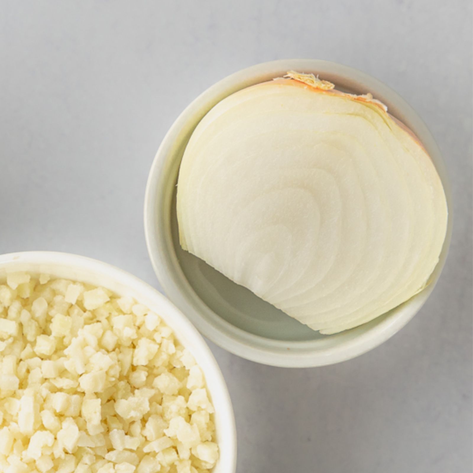 a yellow onion in a white bowl with riced frozen cauliflower out of frame in another white bowl