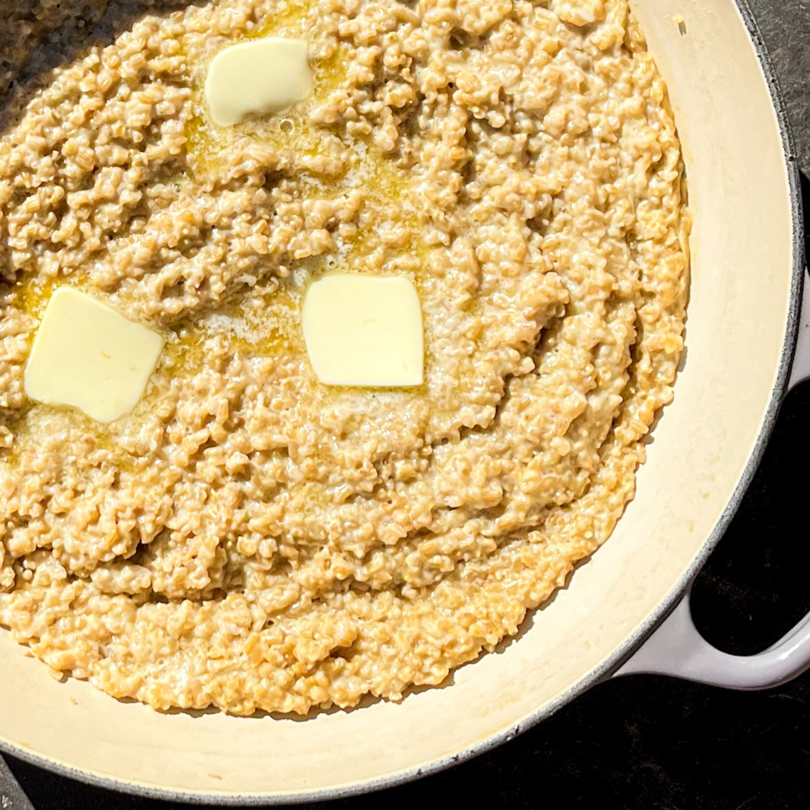 Creamy Oatmeal in a skillet with 3 butter pats