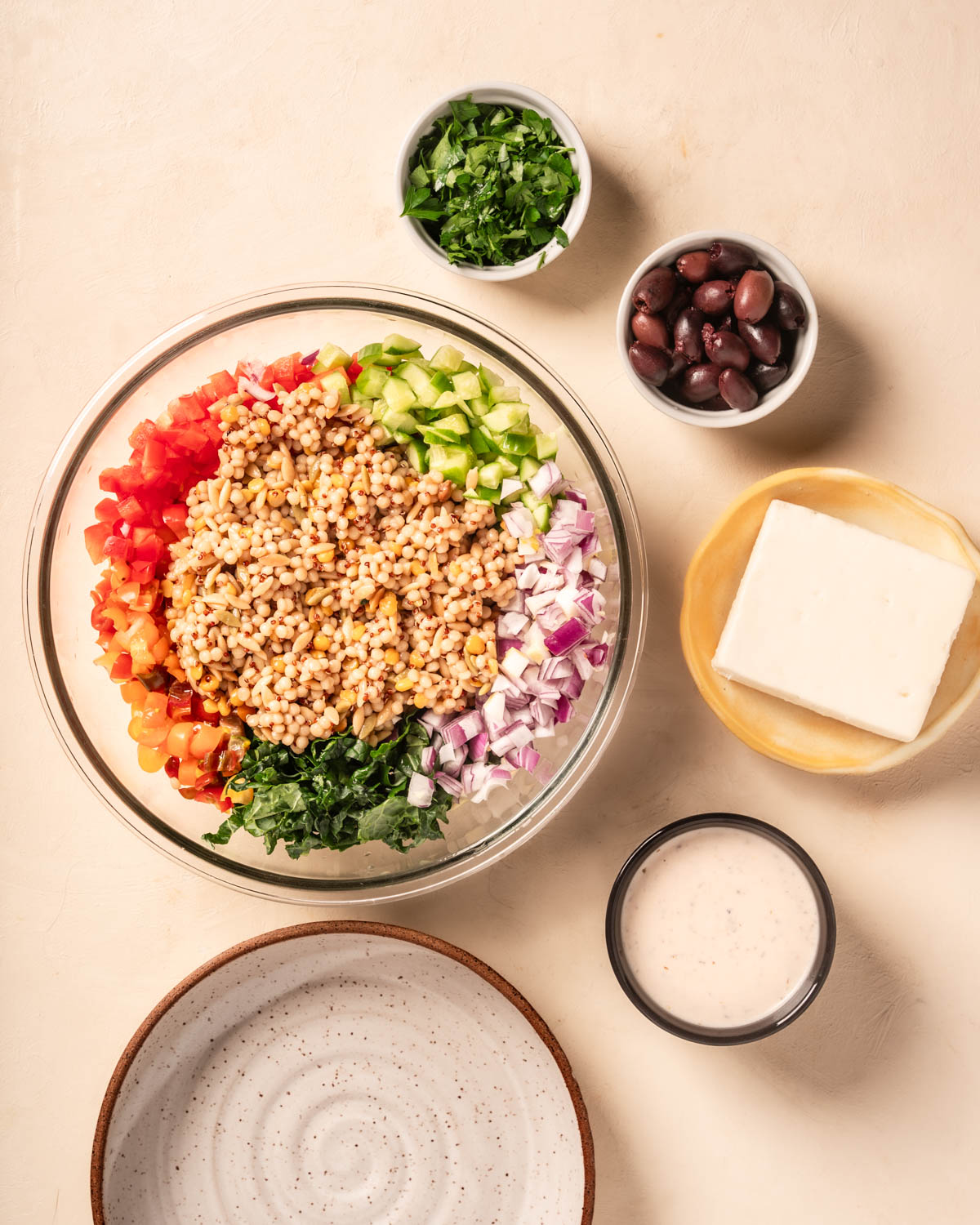 Ingredients for a grain bowl with a large bowl filled with grains and veggies. To the right are smaller plates and bowls with other colorful ingredients.