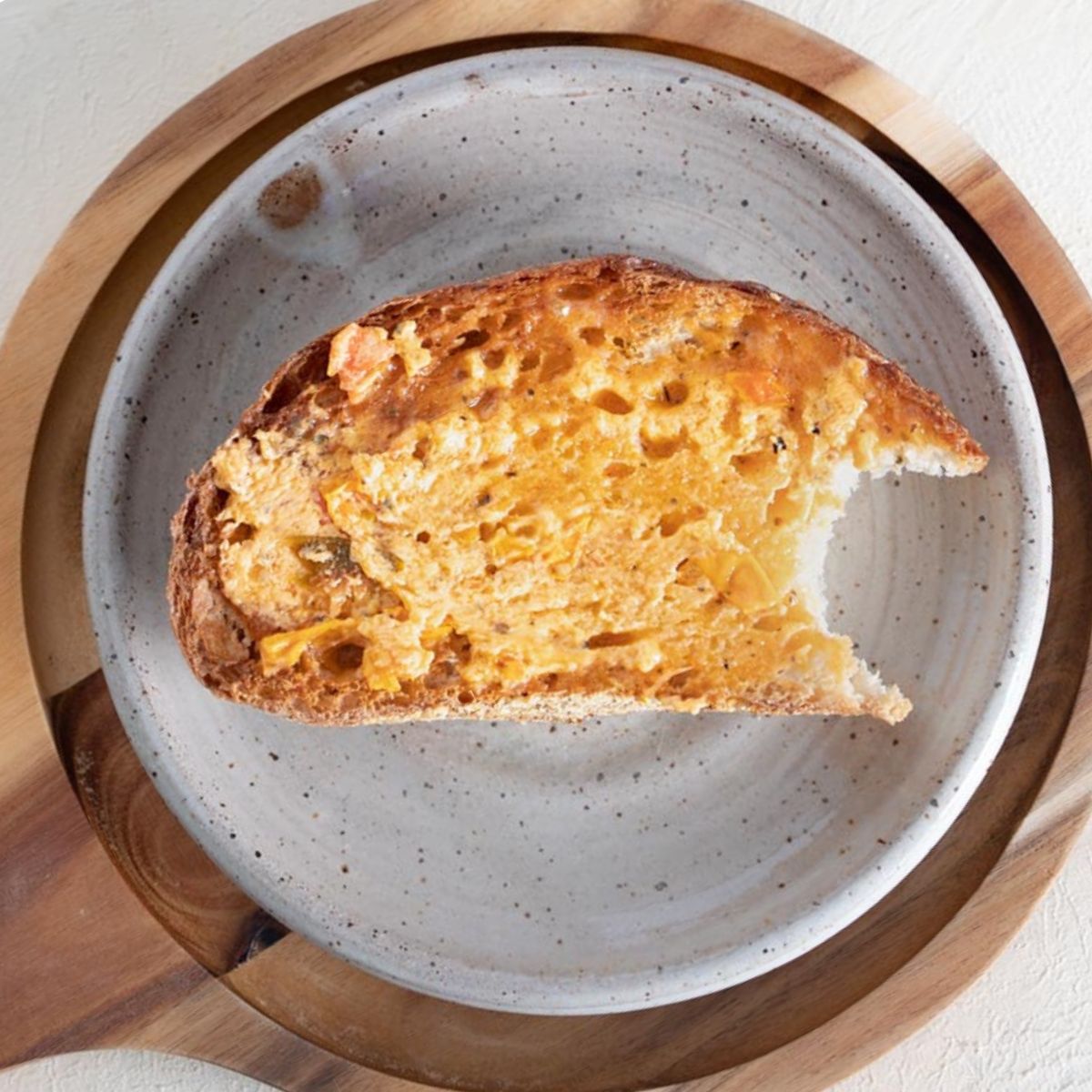 Tomato herb butter smeared on a piece of crust sourdough bread placed on a speckled stoneware plate on a circular brown serving platter