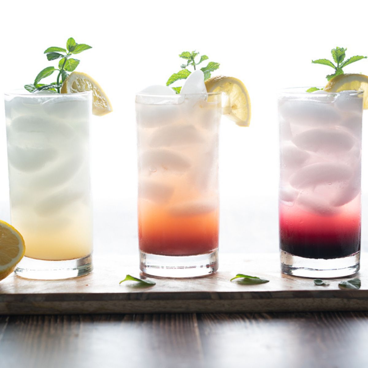 Three mocktails with sprite made with yellow, orange-ish pink, and purple flavorings.