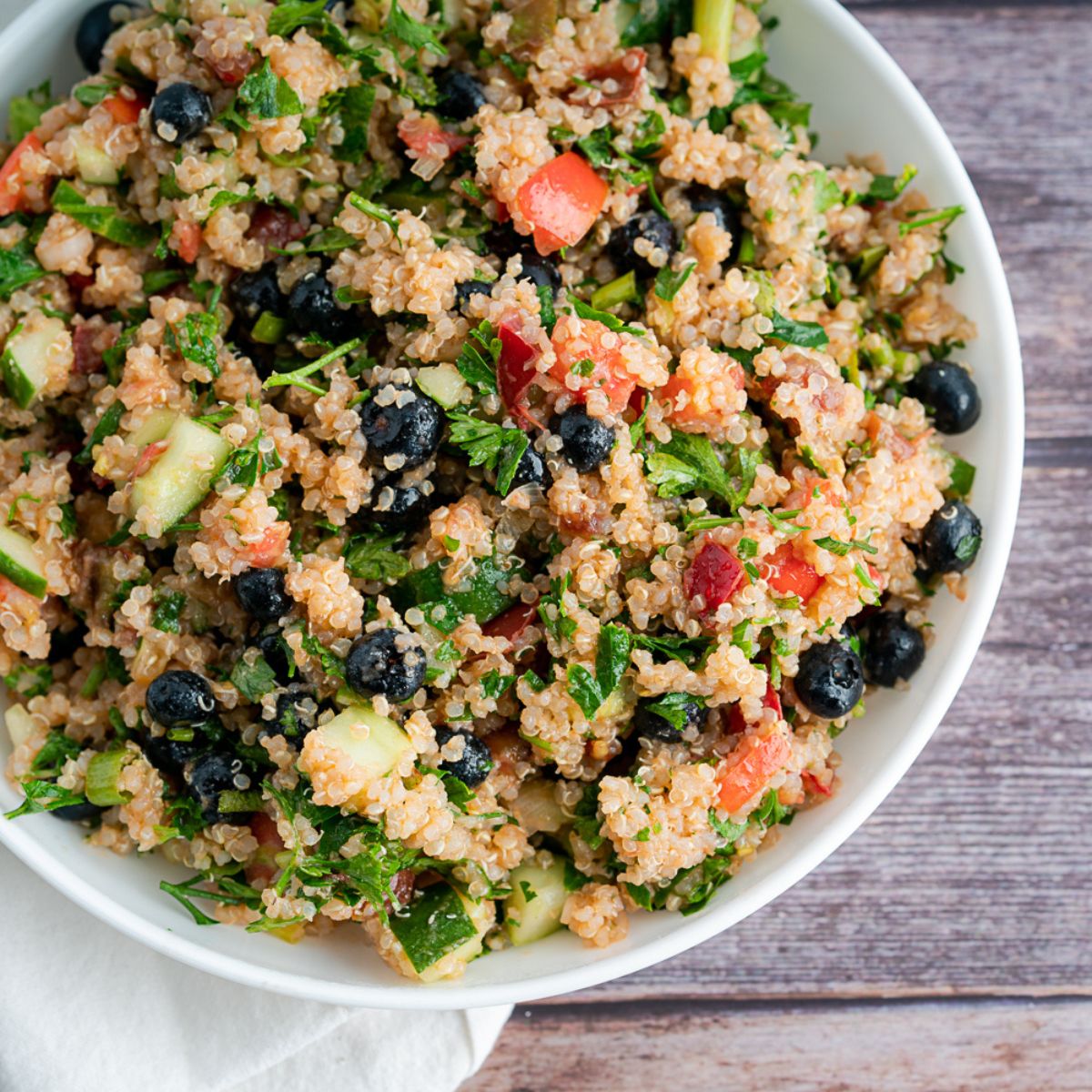 Vegetable Quinoa Recipe With Blueberries in a white bowl and a white linen napkin