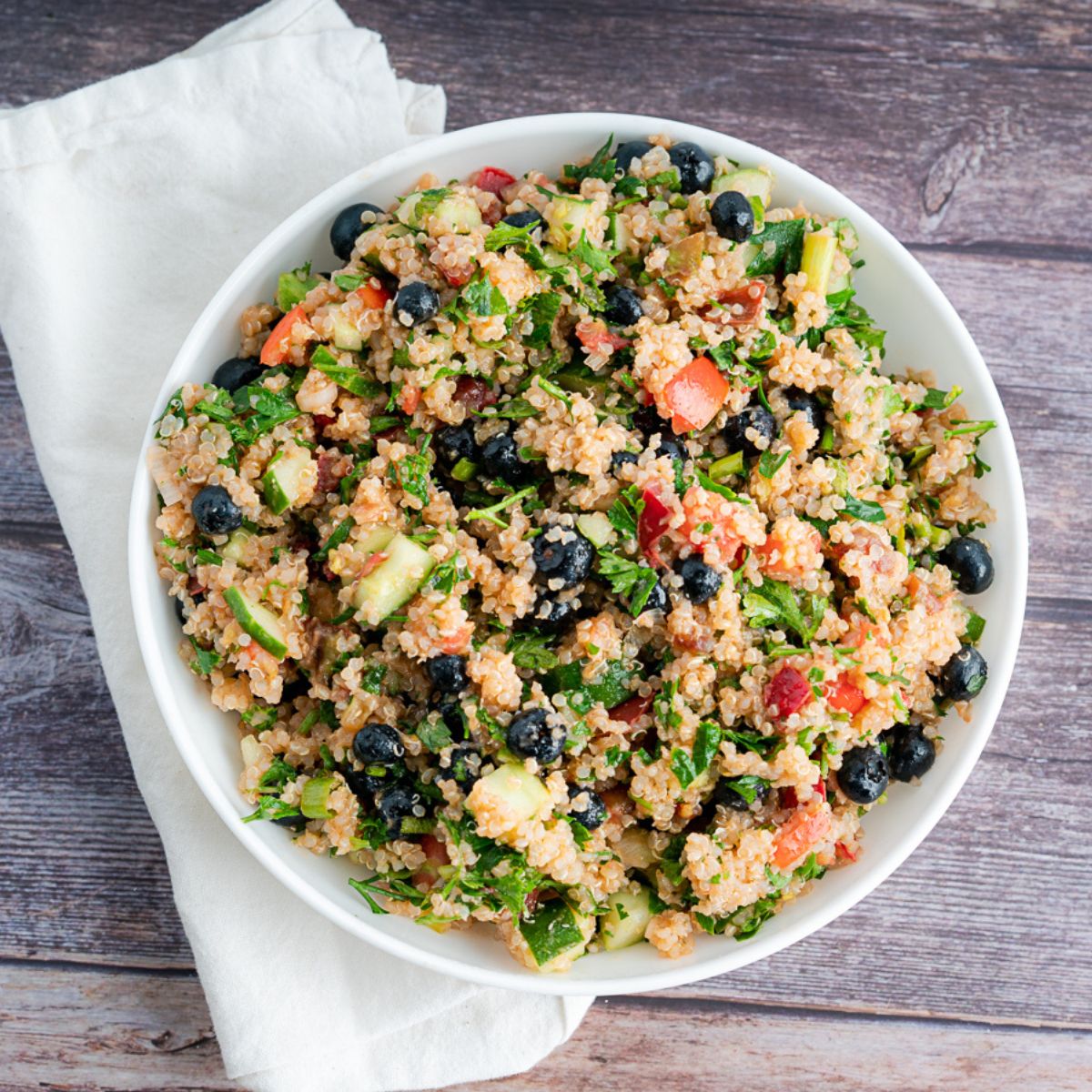 Vegetable Quinoa Recipe With Blueberries in a white bowl and a white linen napkin and wooden backdrop