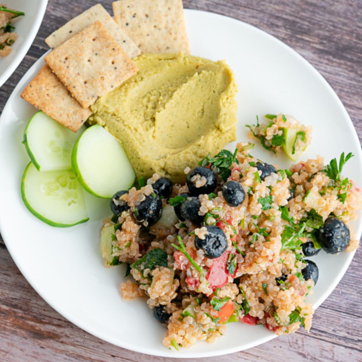 Vegetable quinoa with hummus on a plate with crackers and cucumber