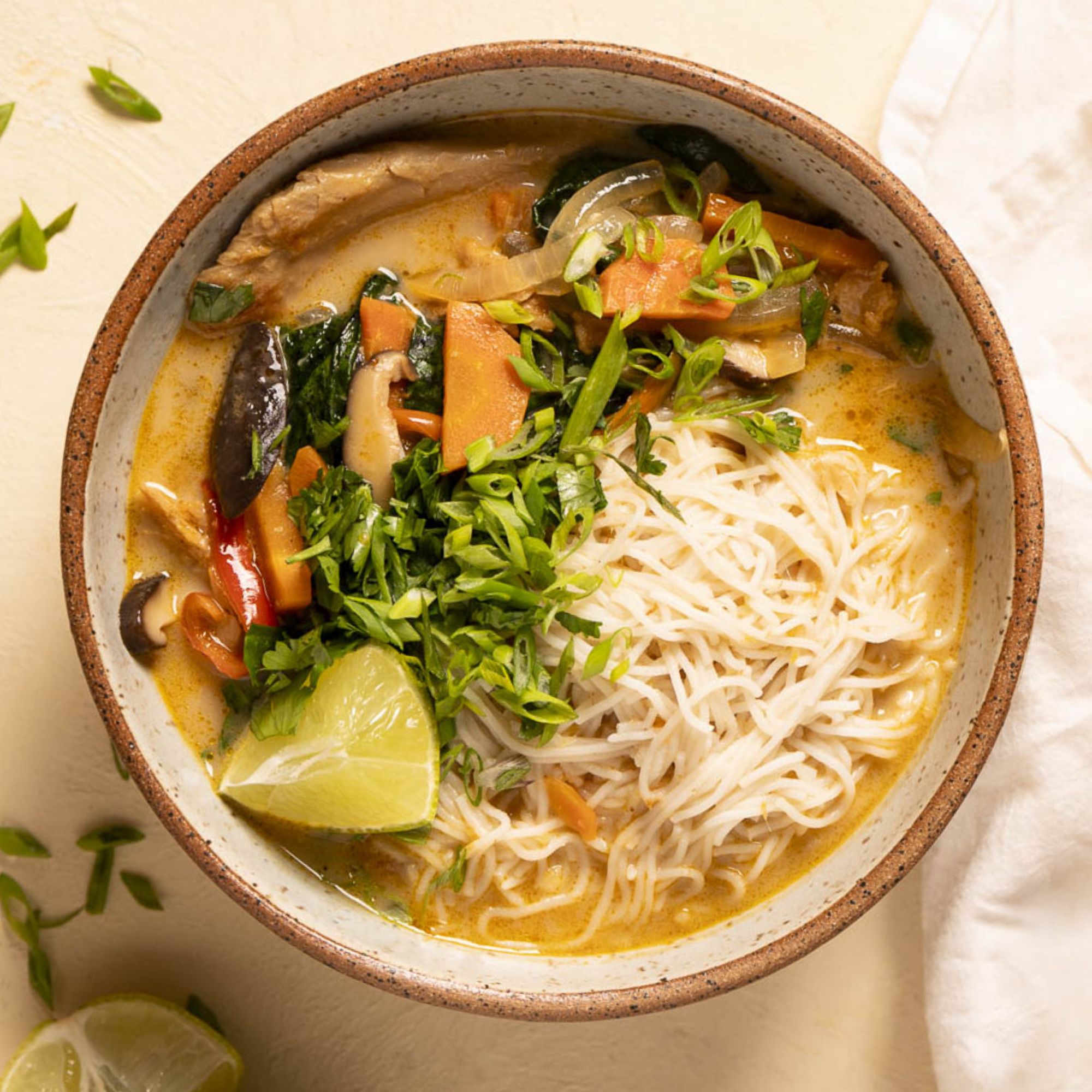 A close up of a stoneware bowl of Panera Thai Chicken Soup Copycat with vegan chicken and vegetables visible in the bowl