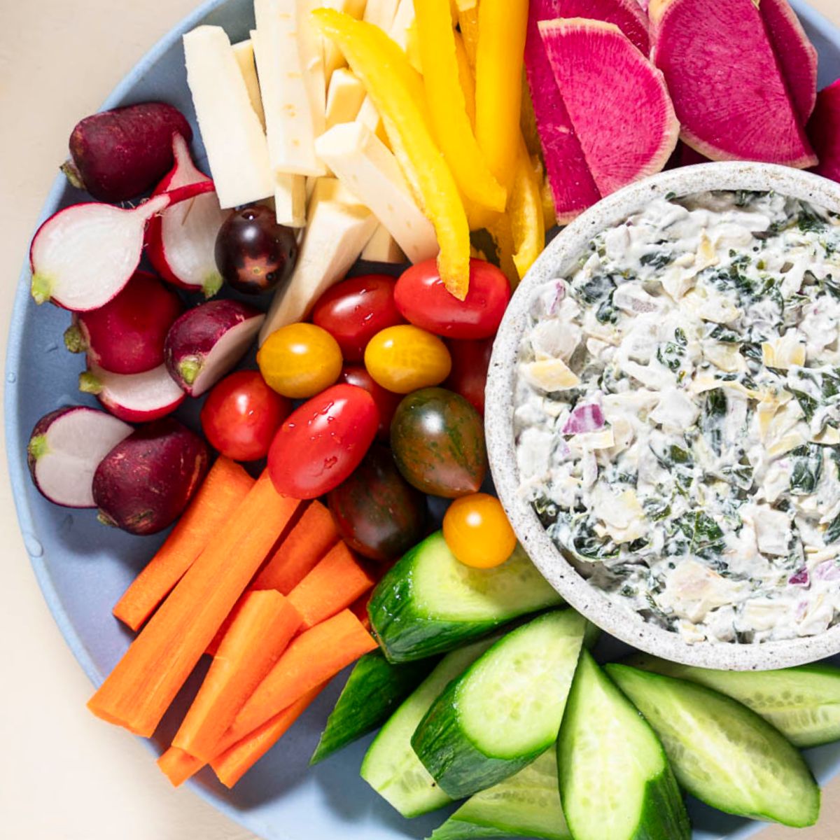 colorful veggie dippers on a blue plate with spinach artichoke dip